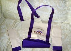 a purple and white tote bag sitting on top of a bed next to a pillow