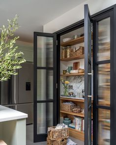 an open pantry with glass doors and baskets on the floor next to a counter top