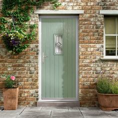 a green front door on a brick building with potted plants and flowers next to it