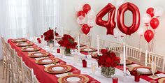 the table is set with red and white plates, silverware, candles, and balloons