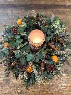 an arrangement of greenery and candles on a wooden table with a candle in the center