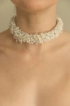 a woman wearing a white necklace with flowers on the neck and chest, close up