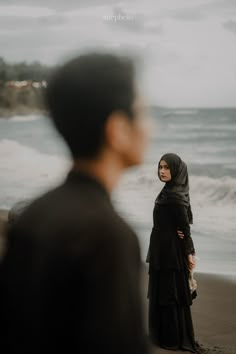 a woman standing on top of a beach next to the ocean with her head covered