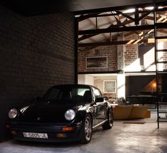 a black car parked in a garage next to a brick wall and ladder on the ceiling