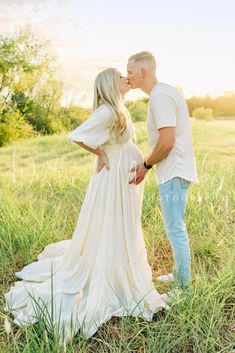 a pregnant couple kissing in a field at sunset