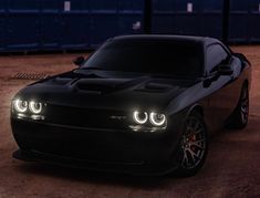 a black sports car is parked in the dirt at night with its headlights turned on