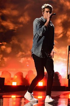 a male in a blue shirt and black pants is on stage with his hand up to his mouth