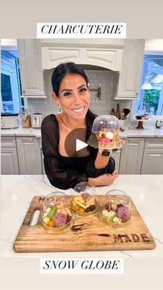 a woman sitting at a kitchen counter holding up a glass bowl filled with salads