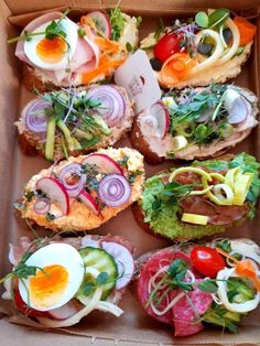 an open cardboard box filled with sandwiches and veggies on top of each other