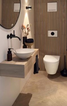 a white toilet sitting next to a bathroom sink under a round mirror on a wall