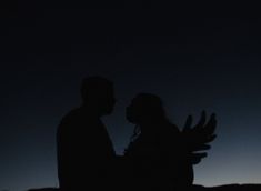 two people are standing in the dark with their arms around each other as they hold hands