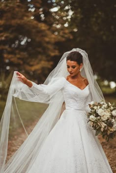 a woman in a white wedding dress holding a bouquet and wearing a long veil over her head