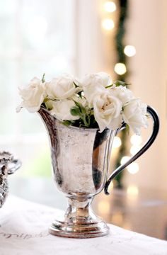 a silver vase filled with white flowers on top of a table