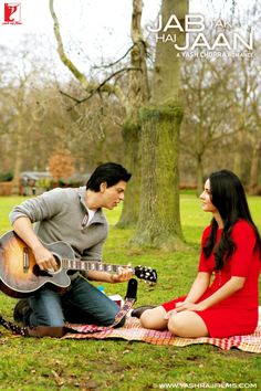 a man playing guitar next to a woman sitting on a blanket in the grass near a tree