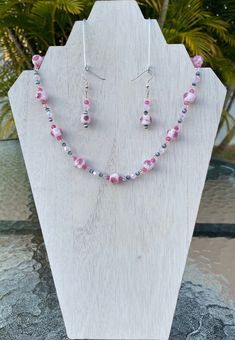 "This pretty necklace set adds a delicate touch to any outfit.  The focus beads in this piece are a light pink with darker pink flowers and some silver striping within them.  These beads are complimented with shiny, light pink bi-cone beads, smaller, clear, light pink bi-cone beads, dark pink round beads, and gray \"cat's eye\" round beads.  The earrings are made with all of the same beads. The necklace measures at about 20 inches long.  It is made on a 49 strand wire.  This means that there are Pink Beaded Czech Glass Jewelry, Adjustable Handmade Pink Jewelry Sets, Pink Jewelry Sets With Matching Earrings As Gift, Pink Czech Glass Necklaces With Colorful Beads, Pink Czech Glass Beaded Necklace For Gifts, Handmade Pink Czech Glass Necklaces, Pink Adjustable Jewelry Sets For Gifts, Handmade Pink Czech Glass Necklace, Elegant Pink Czech Glass Necklaces