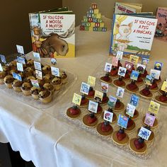 there are many cupcakes on the table with cards and books in front of them