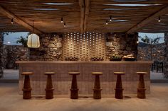 an outdoor bar with stools and stone wall in the background at dusk, lit by lights