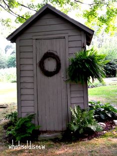 an outhouse with a wreath on the door and plants growing around it, in a yard