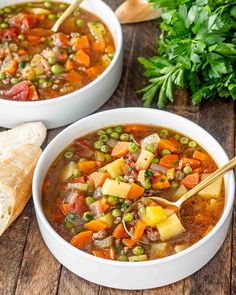 two bowls of vegetable soup on a wooden table with bread and parsley in the background