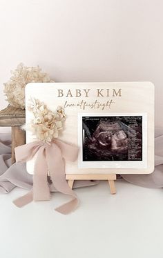 a baby photo frame with a pink ribbon and flowers on the table next to it