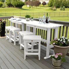 an outdoor table with four stools on a deck next to potted plants and wine bottles