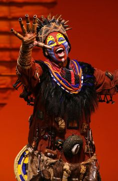 a man dressed in an elaborate costume and headdress, holding his hands up