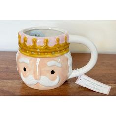 a ceramic mug with a gold crown on it's head sitting on a wooden table