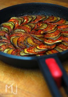 an iron skillet filled with cooked vegetables on top of a wooden table next to a pair of tongs