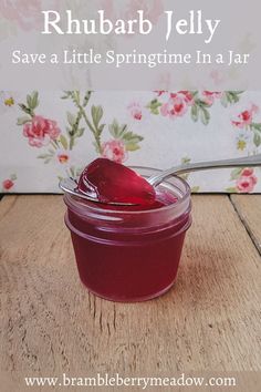 a jar filled with jelly sitting on top of a wooden table next to a spoon