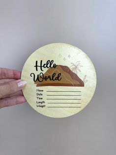 a hand holding a wooden coaster with the words hello world on it and a desert scene