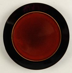 a black and red plate with gold trim on the edge is sitting on a white surface