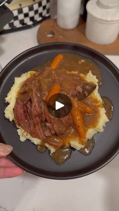 a person holding a plate with meat and mashed potatoes in gravy on it