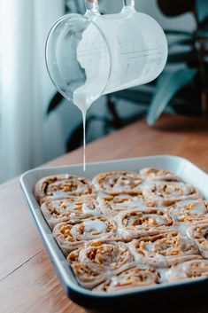 a pan filled with cinnamon rolls being drizzled with icing on top