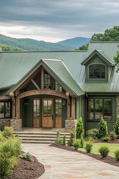 a house with a green metal roof and stone steps leading to the front door is surrounded by greenery