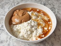 a white bowl filled with food on top of a marble counter next to a spoon