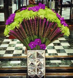 purple and green flowers are in a vase on a checkered tile floor with an ornate fan