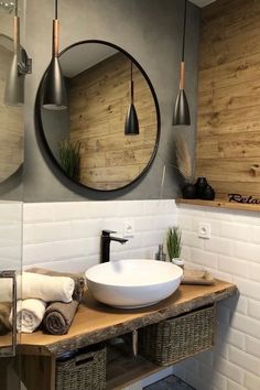 a bathroom sink sitting under a round mirror next to a wooden shelf with towels on it