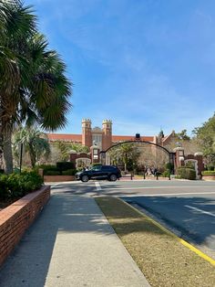 a car is parked in front of a gated entrance to a large building with palm trees