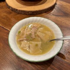 a bowl filled with soup sitting on top of a wooden table next to a spoon