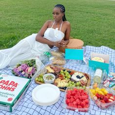 a woman is sitting on the grass with many different types of food in front of her