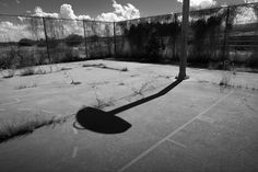 the shadow of a basketball hoop is cast on an empty tennis court in black and white