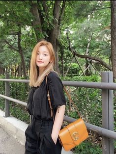 a woman is standing on a bridge holding a brown purse and looking at the camera