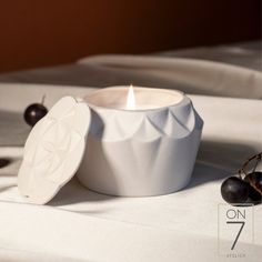 a white candle sitting on top of a bed next to two black cherries in front of it