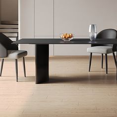 a black table with two chairs and a bowl of fruit on it in front of a white wall