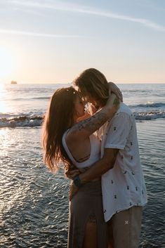 two people standing on the beach kissing each other while the sun sets in the background