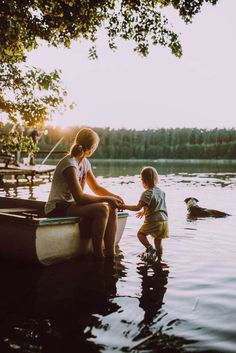 a woman and child are sitting on a boat in the water with a dog nearby