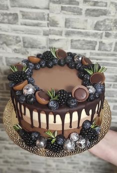 a person holding a cake with chocolate and berries on it