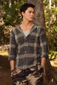 a man standing in front of a tree wearing camo pants and a button up shirt