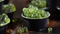 small black bowls filled with green grapes on top of a table