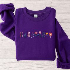 a purple sweater with flowers embroidered on the front and back, sitting on a white wooden surface